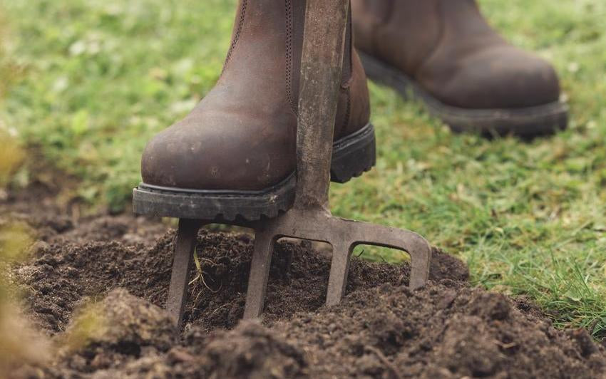 Woman's boot on top of a gardening fork in the ground